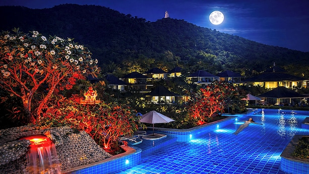 Piscina con cascada, rodeada de árboles iluminados y vistas a la montaña.