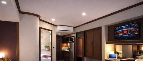 Una habitación de hotel con cama, un escritorio con silla, televisor y kitchenette.