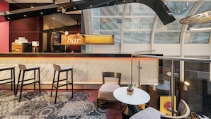 A modern bar area with a glass partition, bar stools, and a seating area with a round table. - Ikonik Parlament (Budapest)