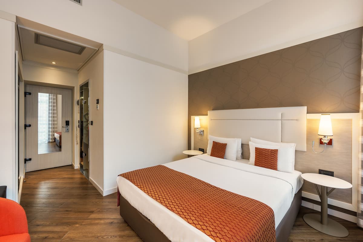 Habitación de hotel con una cama grande, dos mesitas de noche, un espejo y un diseño de pared moderno.