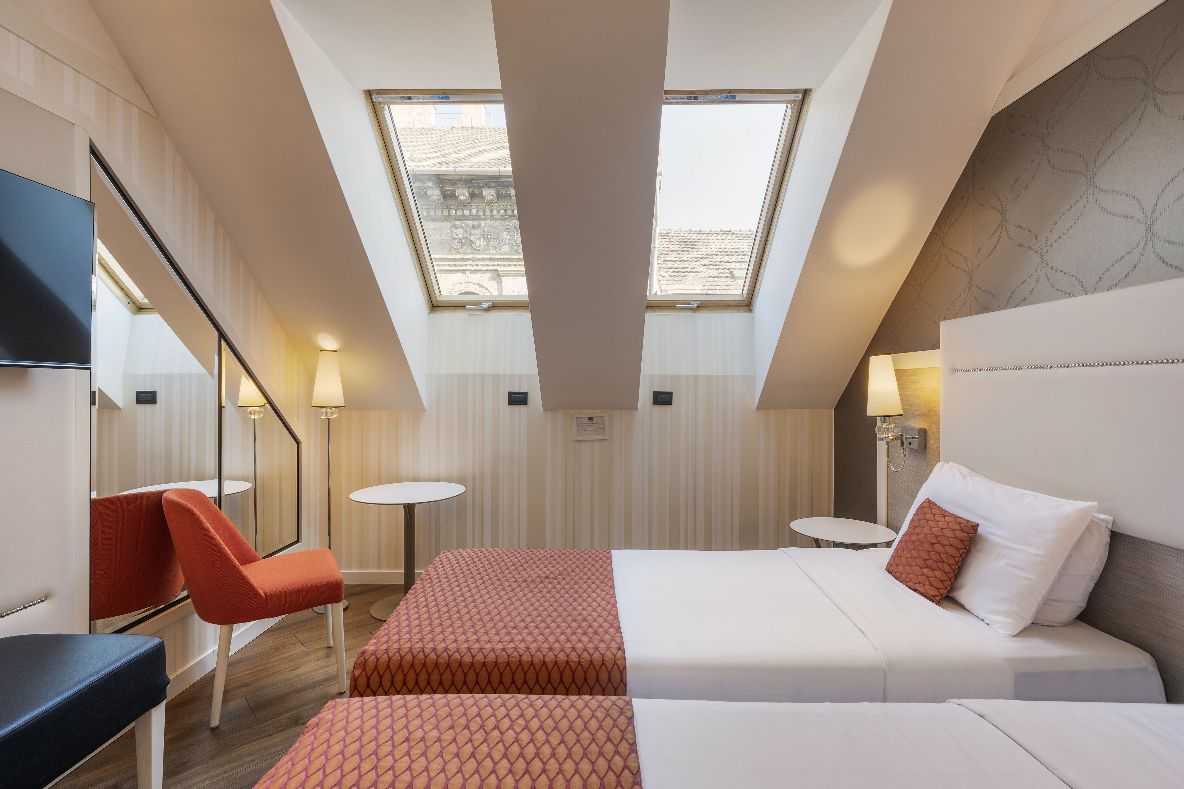 Una habitación de hotel con tragaluces, una cama, un escritorio y una silla.