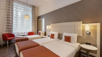 A hotel room with two beds, a red chair, a small table, and a wall-mounted lamp.