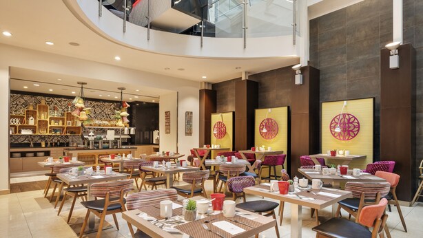A modern dining area with multiple tables and chairs, a kitchen in the background, and decorative wall art. - Ikonik Parlament (Budapest)