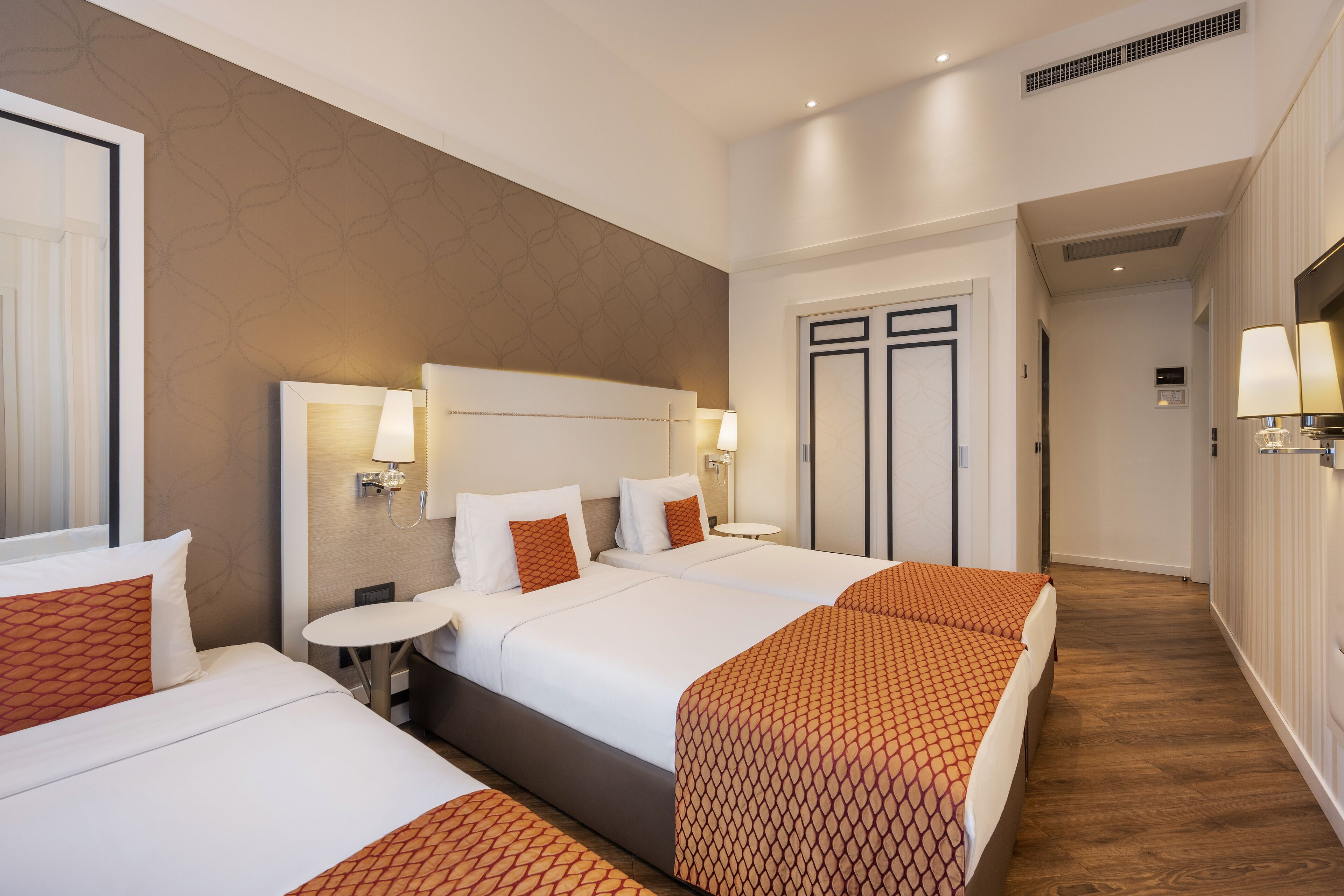 A hotel room with three beds, a small round table, and a bathroom with a mirror and towel rack.
