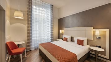 Une chambre d’hôtel moderne avec un grand lit, une chaise, une petite table et une fenêtre avec des rideaux légers.