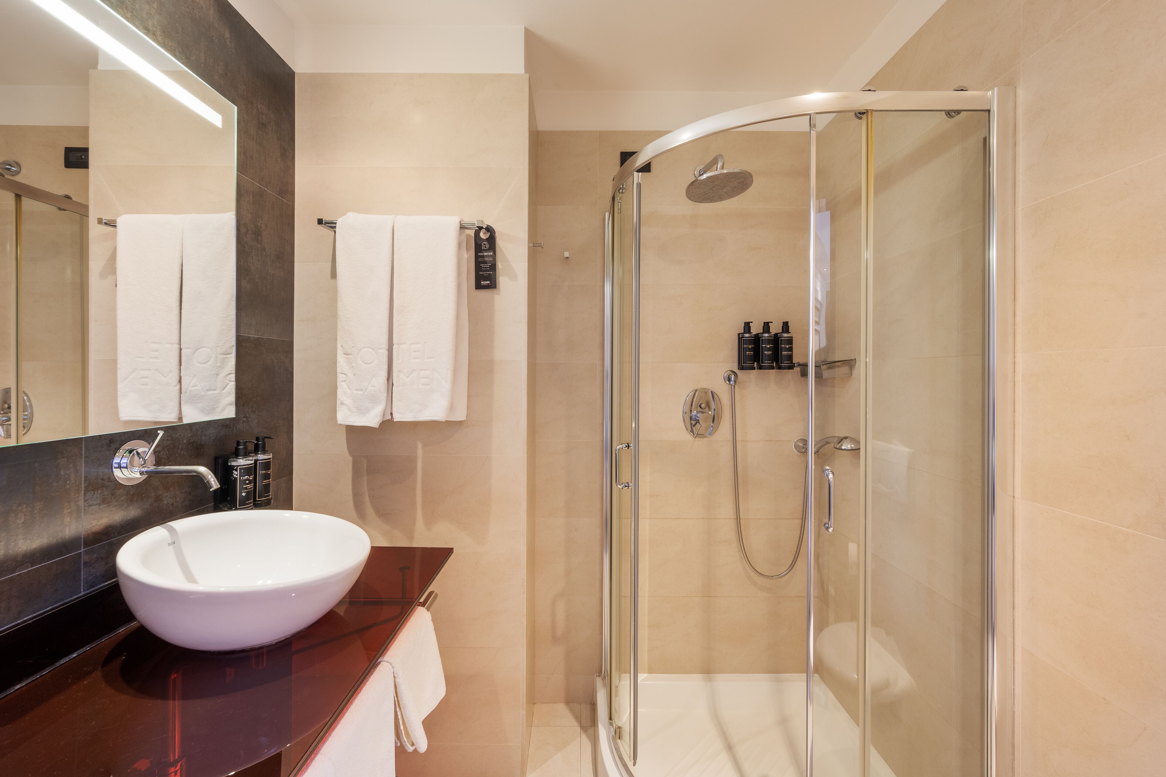 Un baño moderno con ducha envuelta en vidrio, un lavabo blanco y un espejo grande.