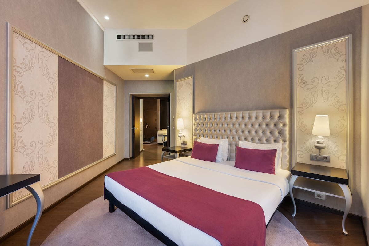 Habitación de hotel con una cama grande, una mesita de noche con lámpara y vistas al pasillo.