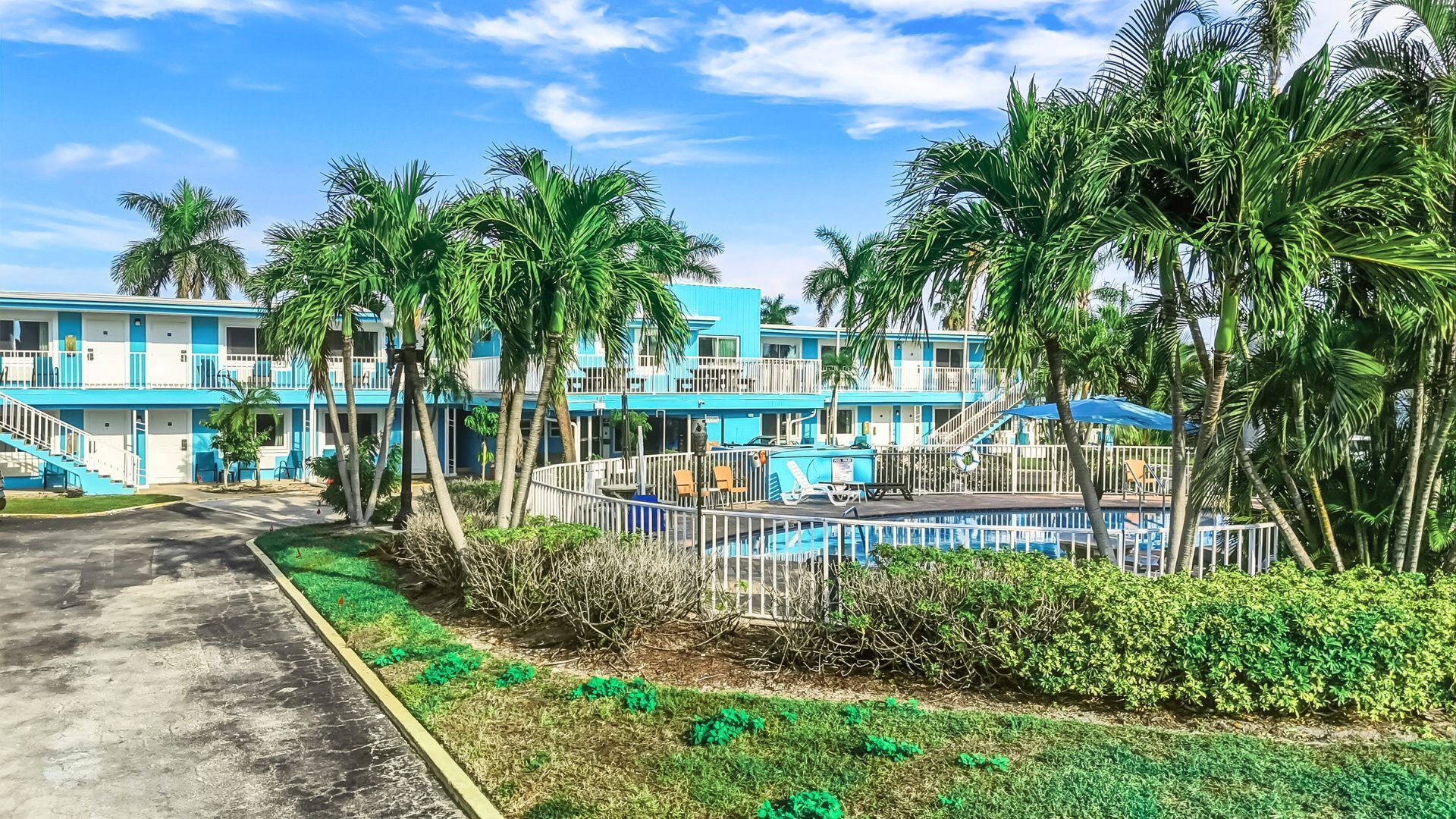 Motel blau amb piscina, envoltat de palmeres i vegetació.