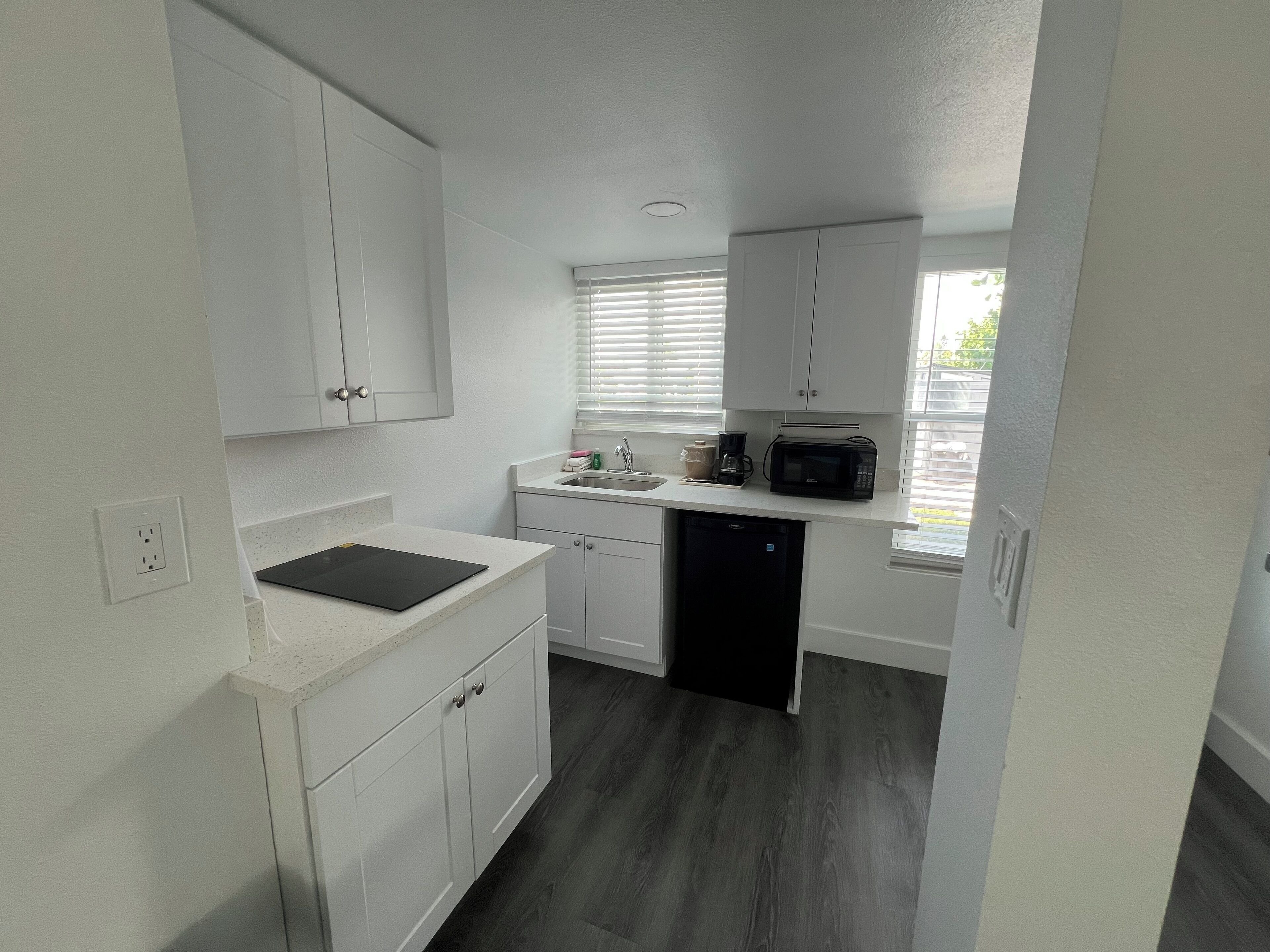 A compact kitchen with white cabinets, a black countertop, and a dishwasher.