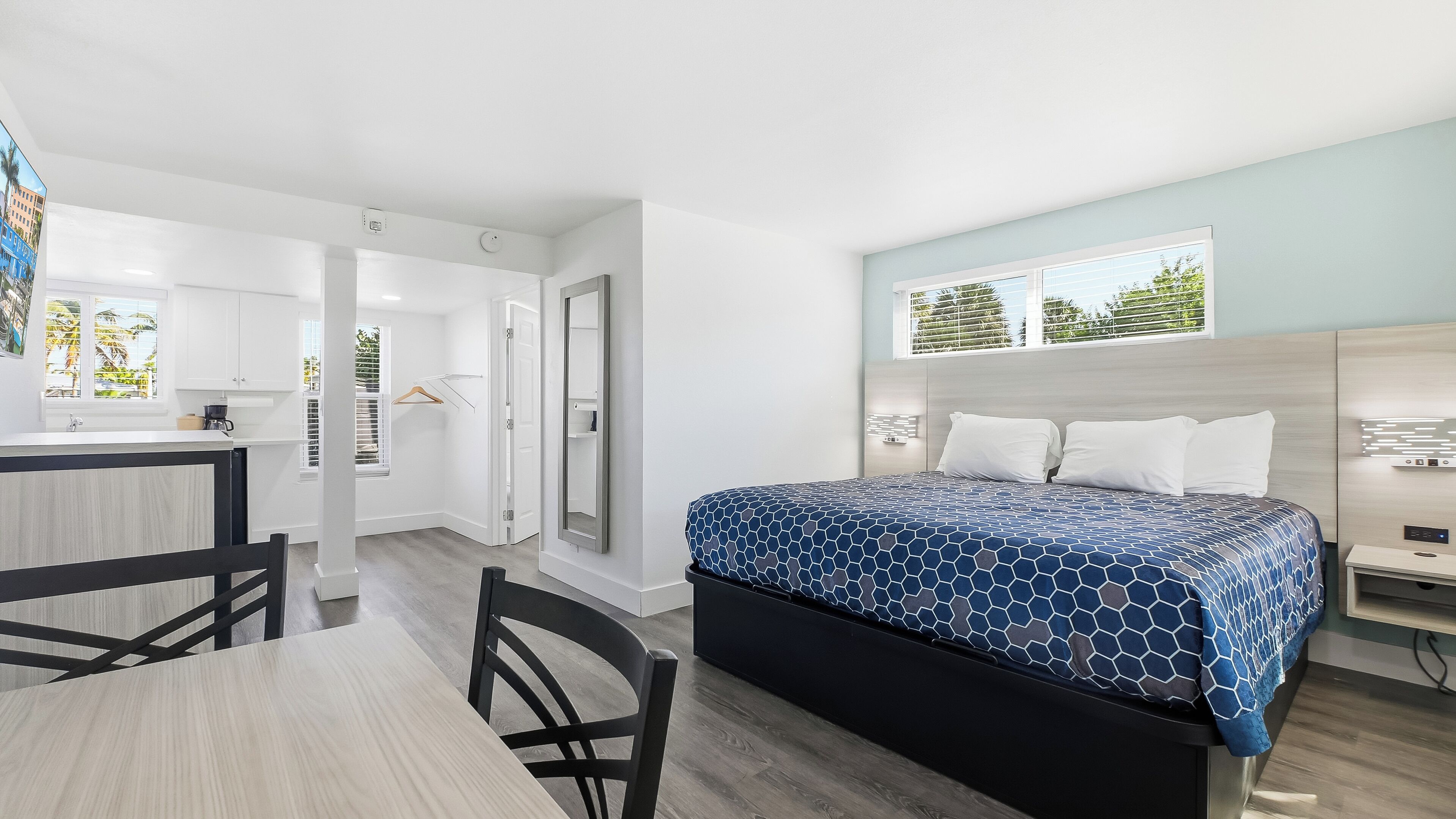 Una habitación de hotel moderna con una cama, un escritorio y una silla. Se ve una ventana con vistas a palmeras.