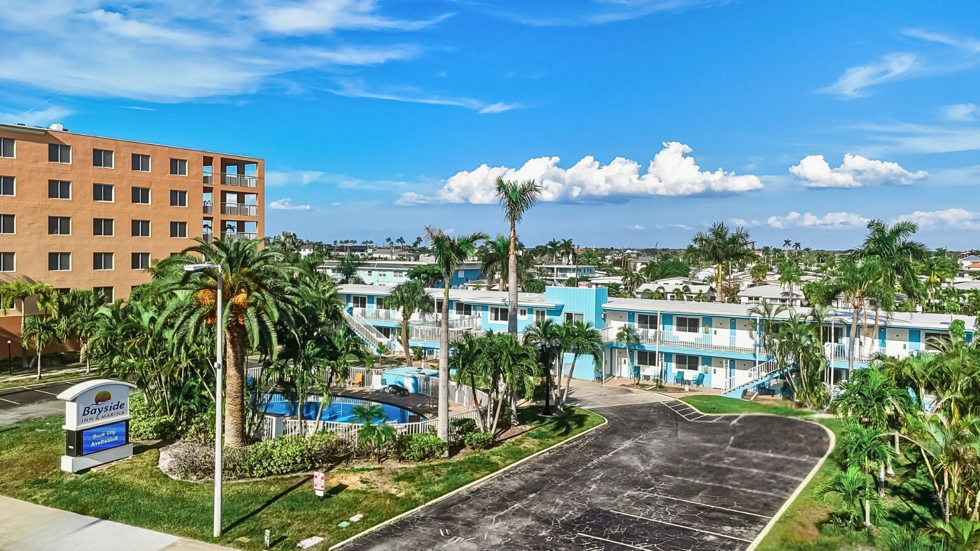 Een hotel met een zwembad, palmbomen en een bord met daarop Bayside Inn & Marina.