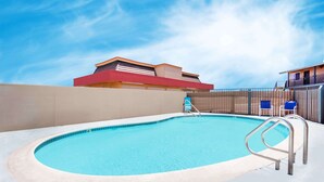 Una piscina con una escalera de metal, rodeada por un muro color crema y una cerca.