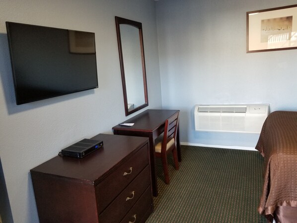 Habitación de hotel con televisión de pantalla plana, un espejo, escritorio con cajones, aire acondicionado y una cama.