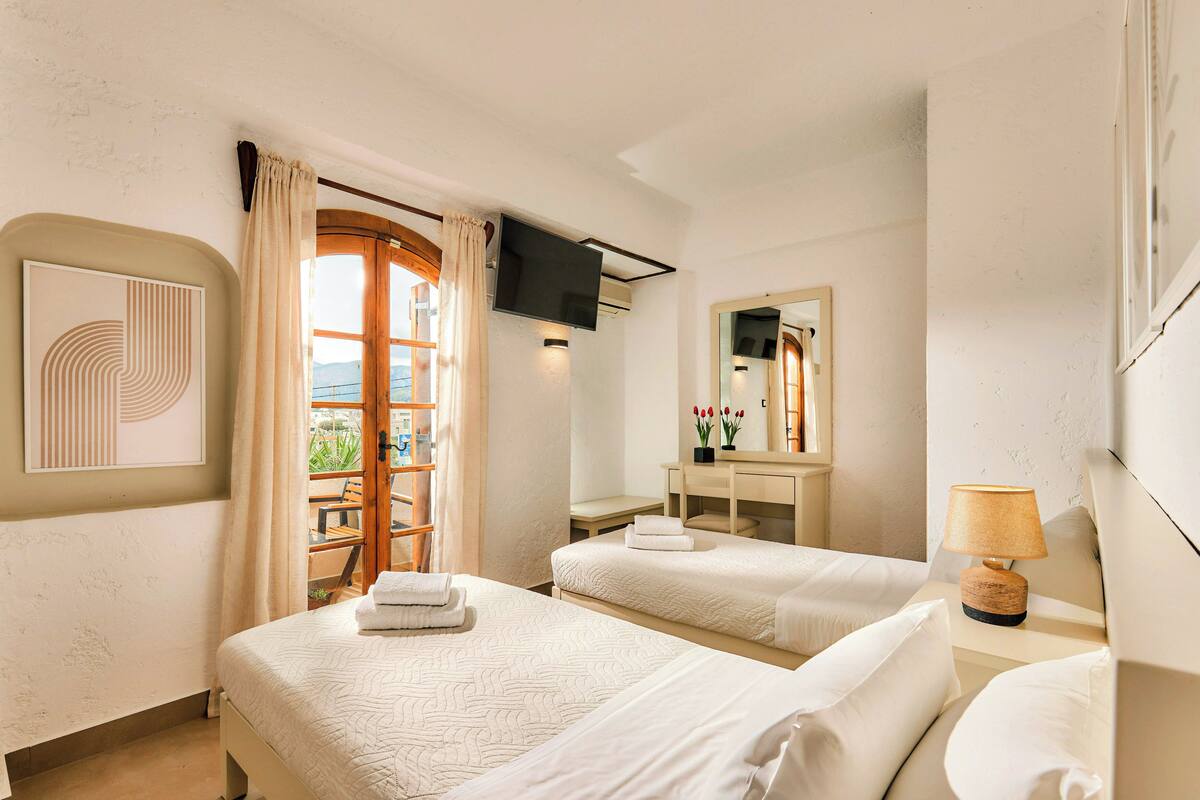 Een hotelkamer met twee bedden, een televisie, een bureau met een lamp en uitzicht op het omliggende landschap.
