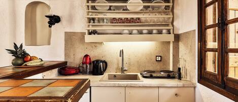 A kitchen with a marble countertop, a sink, and a shelf above the counter holding dishes and glasses.