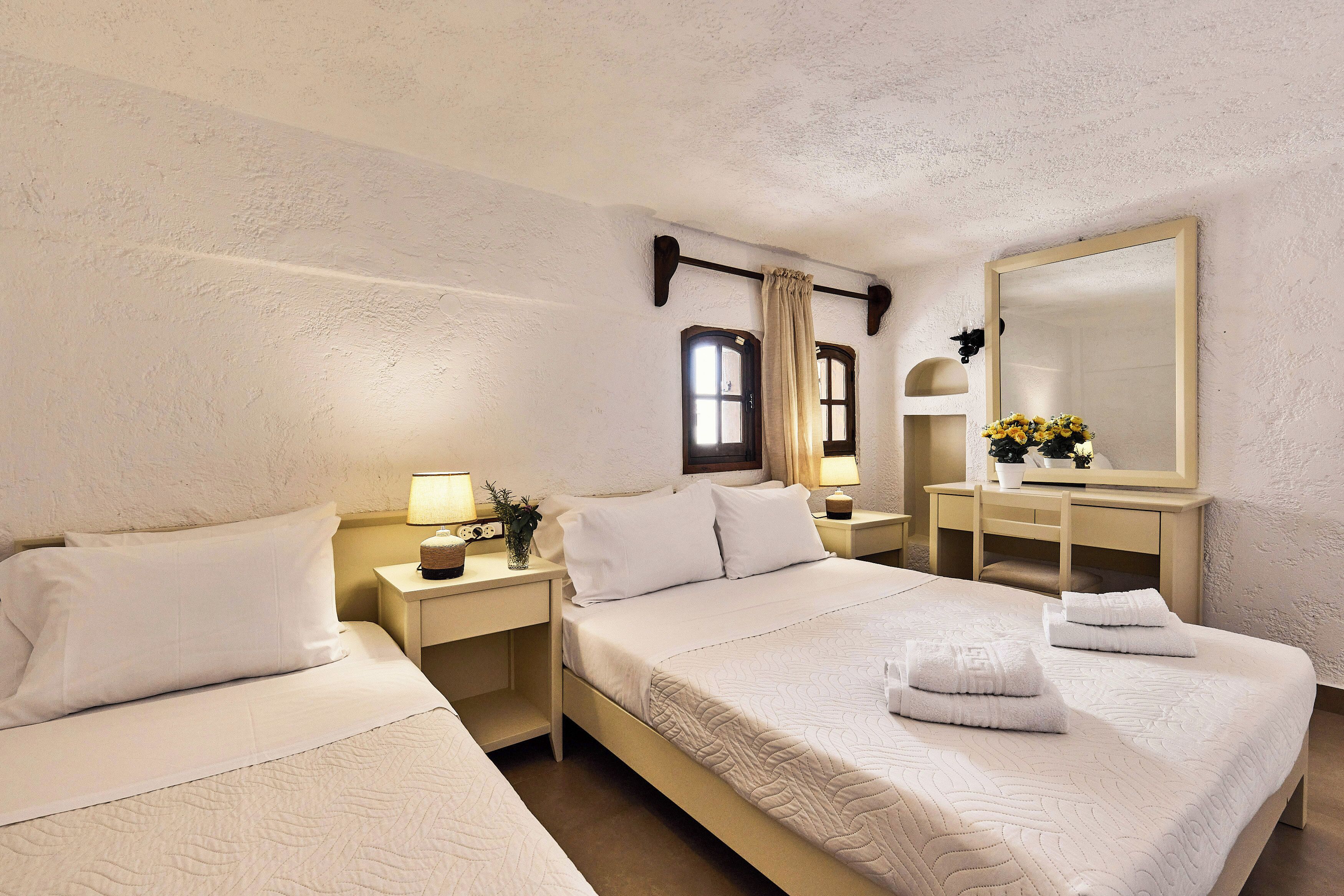 A hotel room with two beds, a large mirror, a bedside table with a lamp, and a window with curtains.