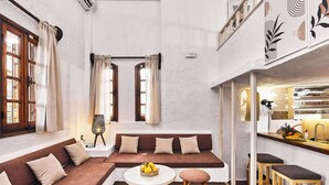 A cozy interior with a brown sofa, a round table, and two bar stools. - Mila Malia Studios Hotel  (Hersonissos)