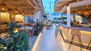 An outdoor cafe with wicker furniture, hanging lights, and a view of the city. - Mila Malia Studios Hotel  (Hersonissos)