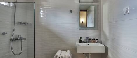 A modern bathroom with a glass-enclosed shower, a sink with toiletries, and neatly folded towels on a stool.