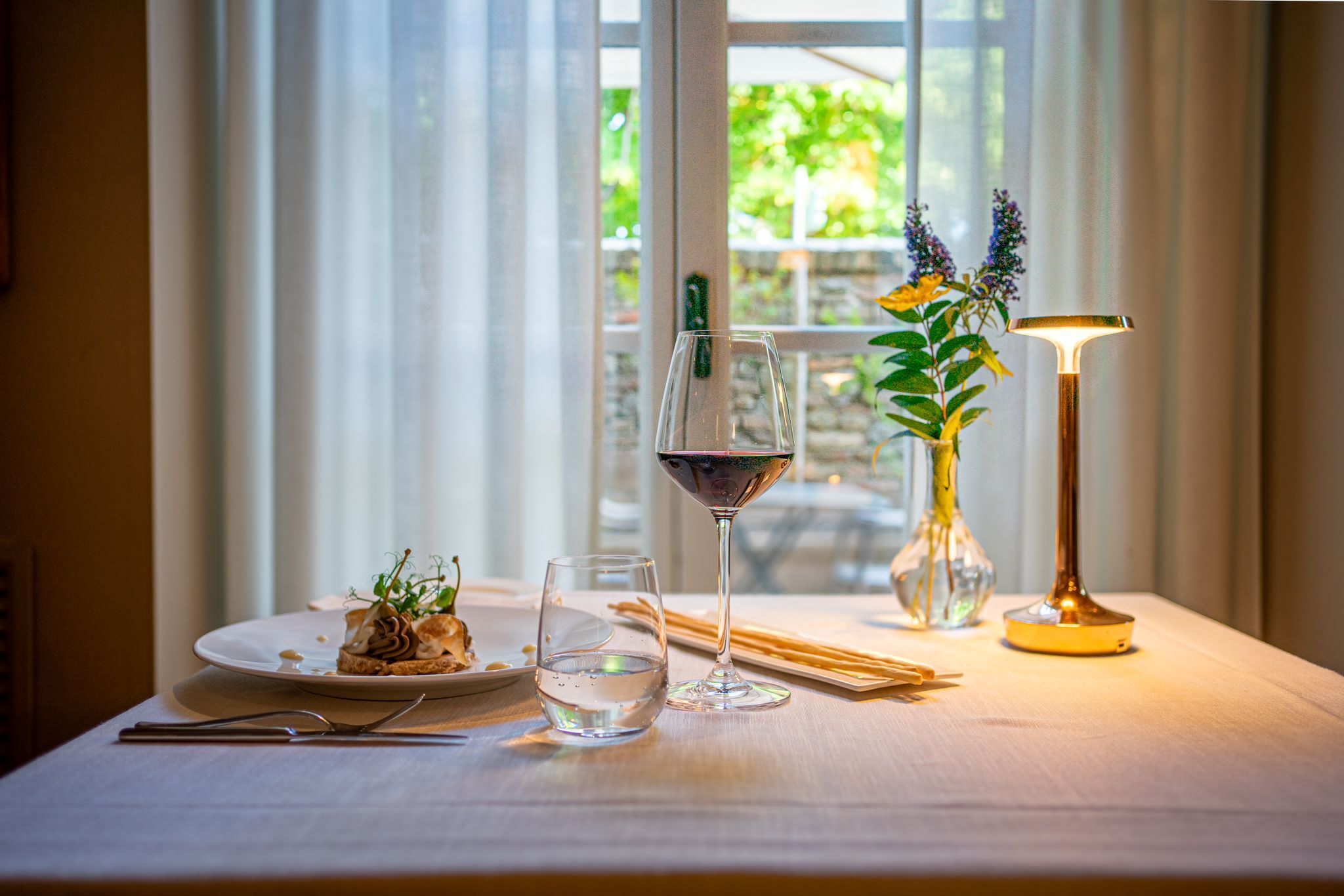 A dining table with a plate of food, a glass of red wine, a glass of water, chopsticks, and a candle.