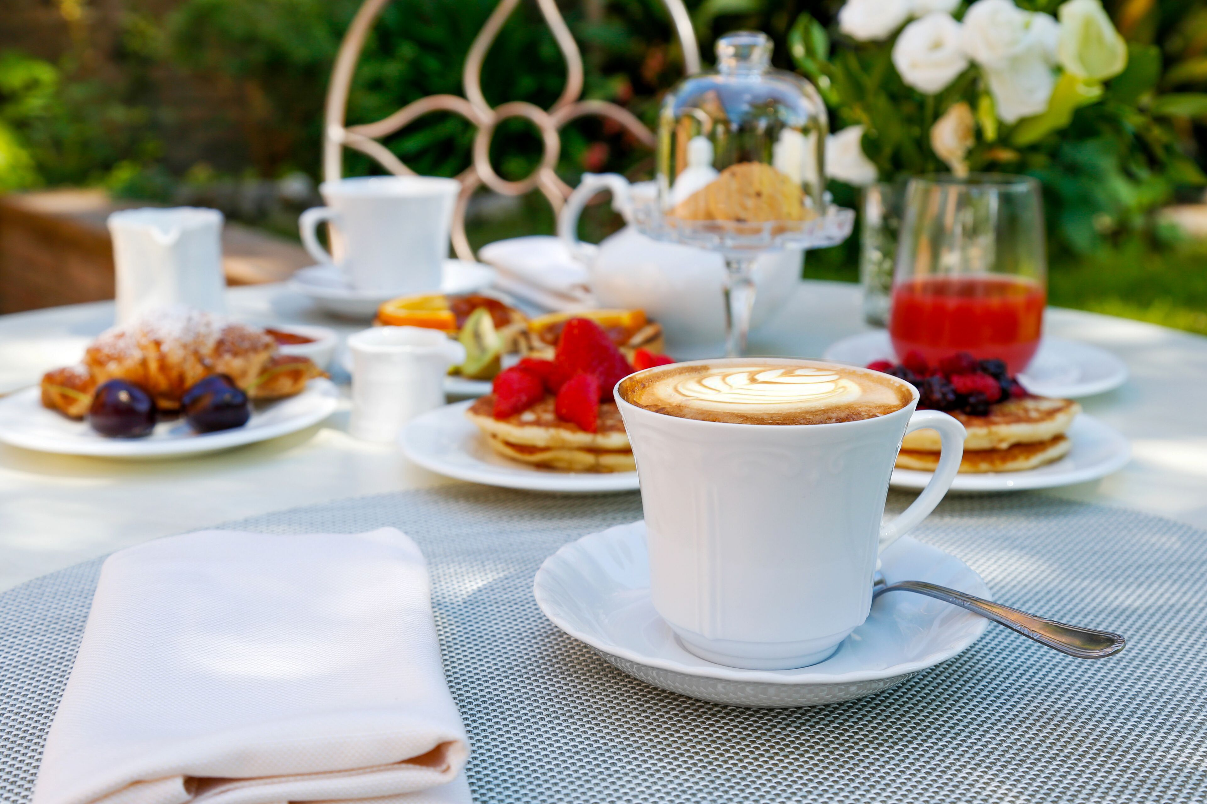 A table set with a cup of coffee, pastries, and a glass of red drink, surrounded by greenery.