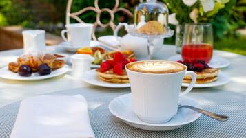 A table set with a cup of coffee, pastries, and a glass of red drink, surrounded by greenery.