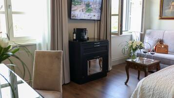 Habitación de hotel con televisión montada en la pared, chimenea, sofá y una mesita con un jarrón de flores.