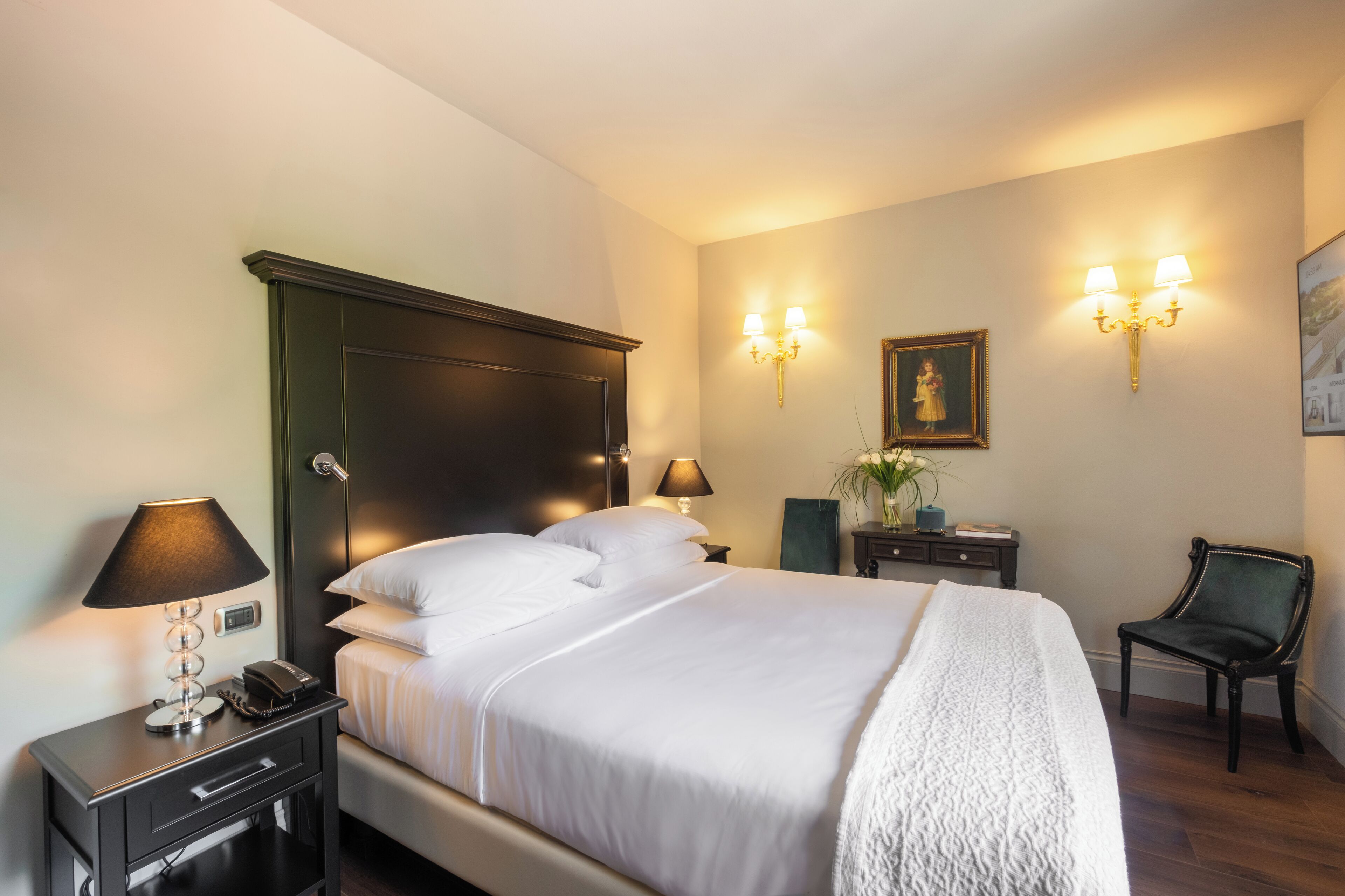 A neatly made bed with white linens, a bedside table with a lamp, a chair, and wall-mounted lamps.