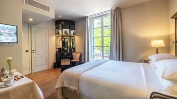 Una camera d'albergo con un letto grande, una scrivania con una sedia, una TV appesa al muro e una finestra con tende.