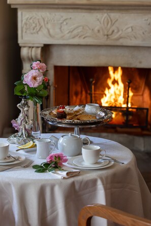 A table set for tea with a tray of pastries, a vase of flowers, and a fireplace in the background. - Hotel Vannucci (Citta della Pieve)