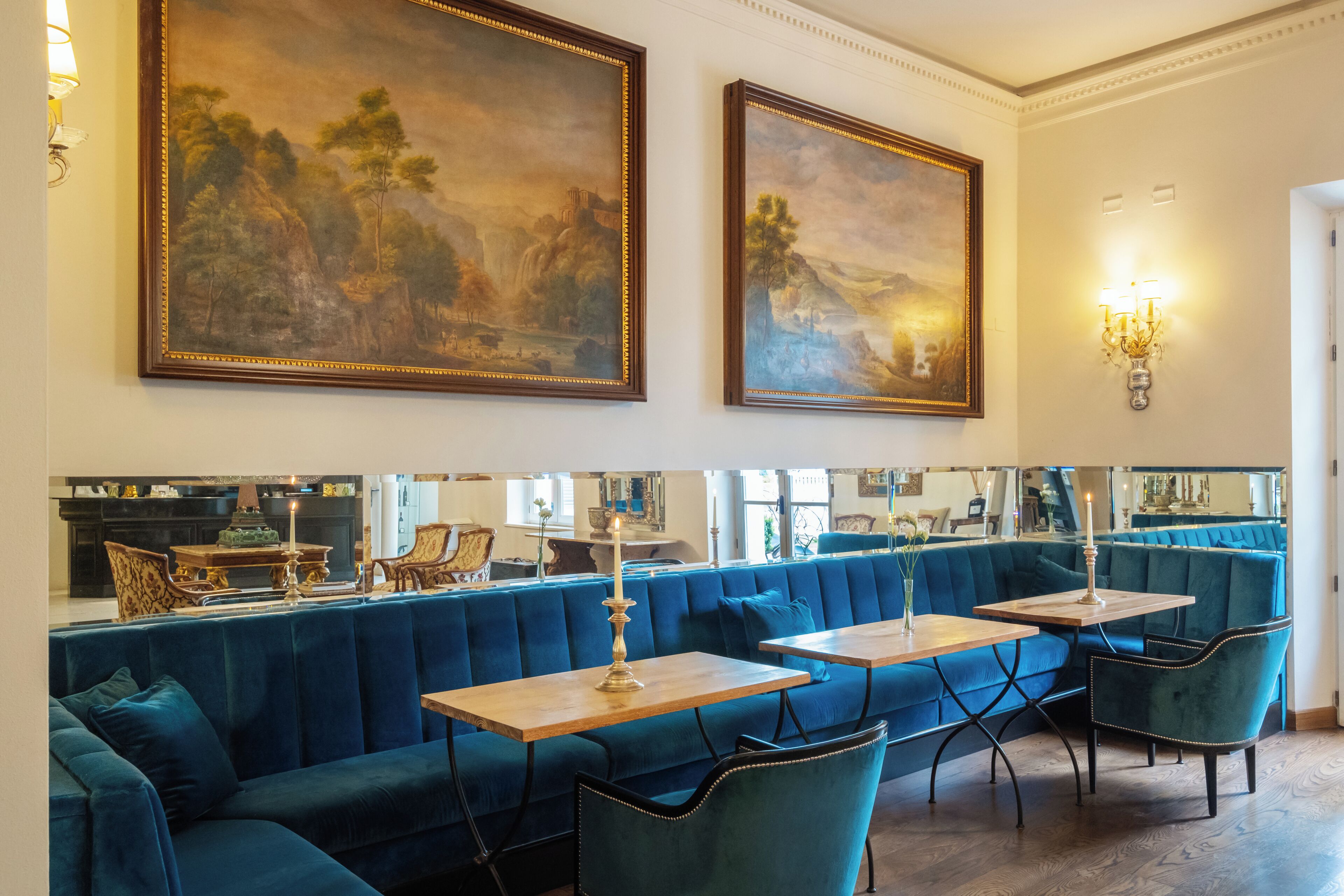 Een restaurant met blauwe fluweelzittingen, houten tafels en grote landschapsprenten aan de muren.