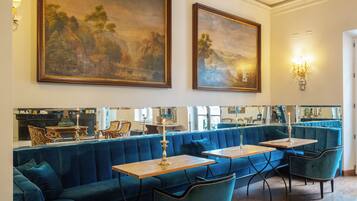 Un restaurante con asientos de terciopelo azul, mesas de madera y grandes pinturas de paisajes en las paredes.