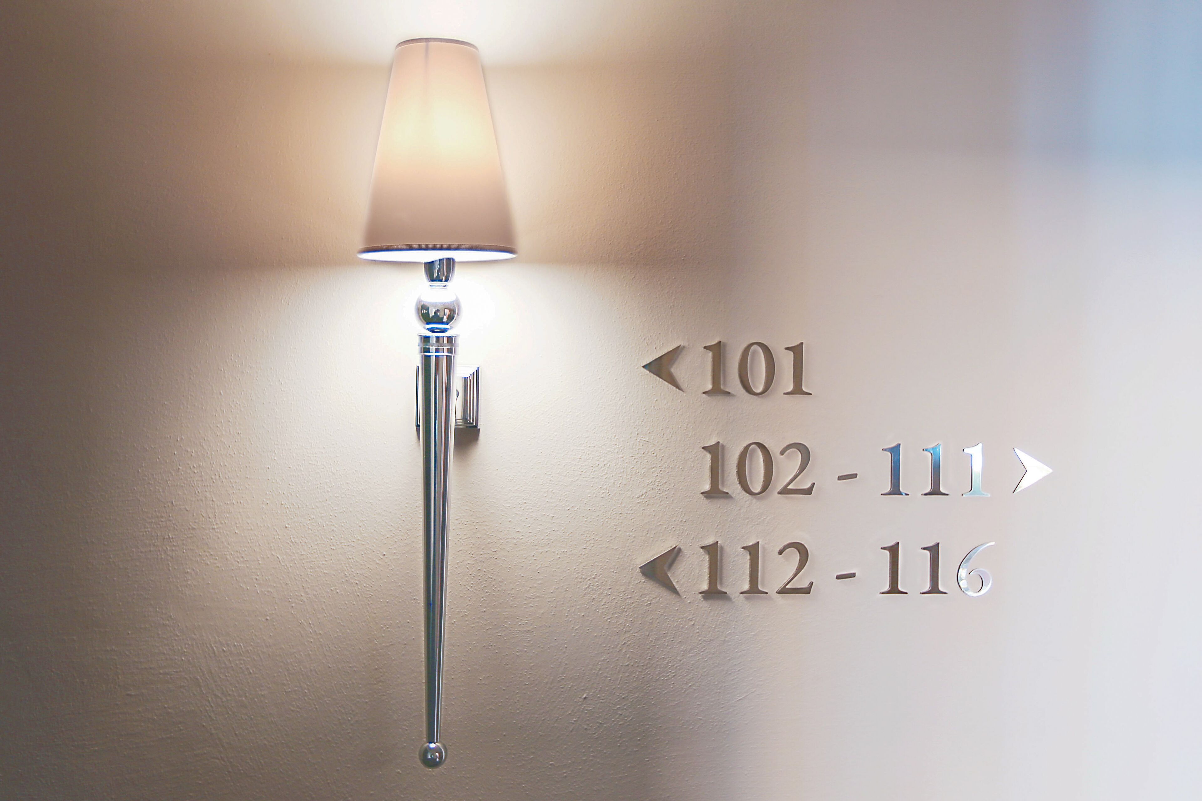 Luminária de parede com setas direcionais indicando os números dos quartos 101, 102 a 111 e 112 a 116.