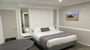 A bedroom with a bed, a bedside table, a chair, a round table, and a painting on the wall. - Pony Express Motel (Jackson)