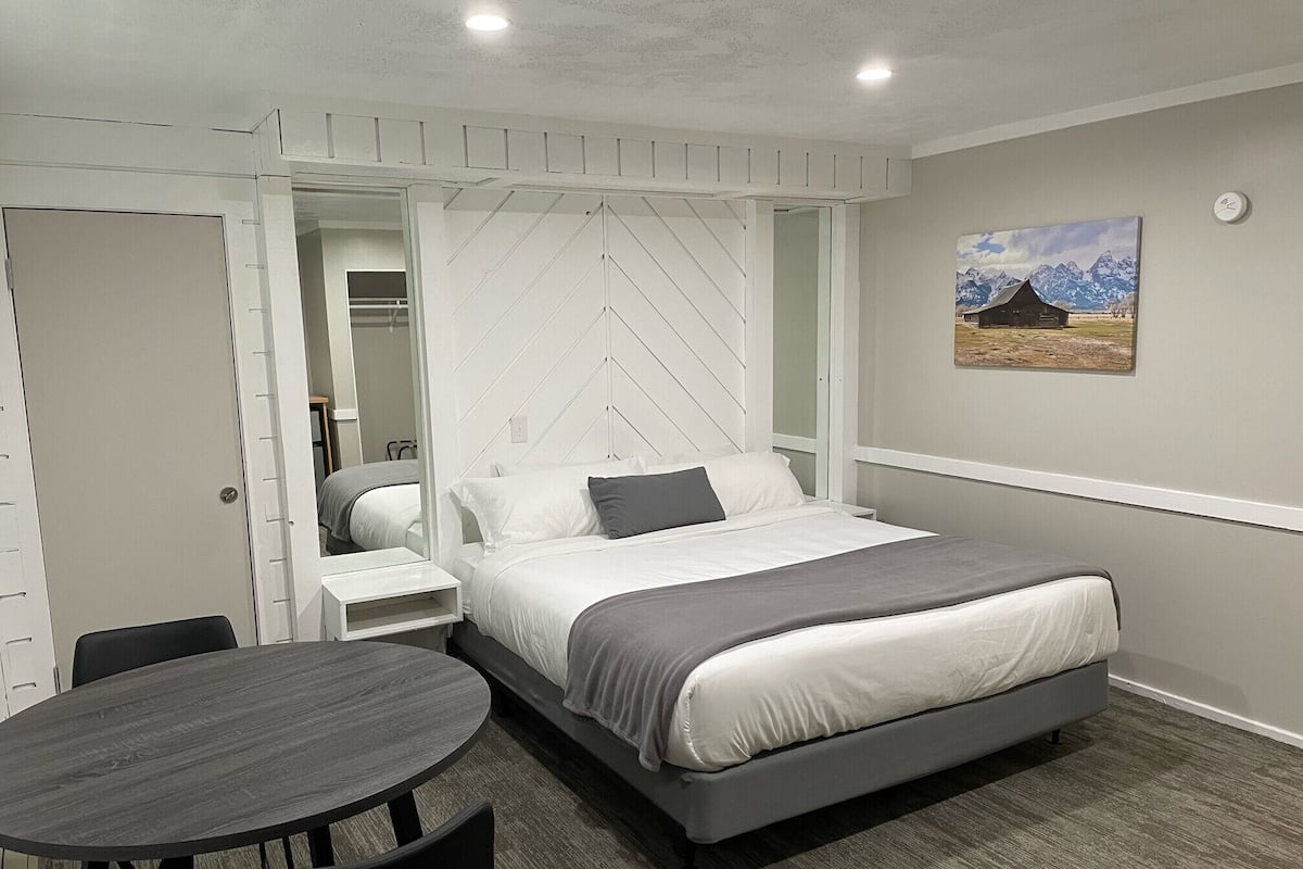 A bedroom with a bed, a bedside table, a chair, a round table, and a painting on the wall.