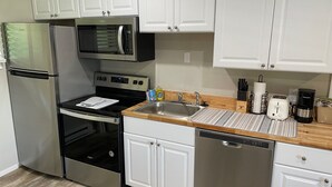 A modern kitchen with stainless steel appliances, white cabinetry, and a wooden countertop. - Pony Express Motel (Jackson)