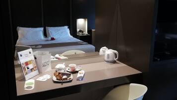 A modern hotel room with a bed, bedside table, and a small seating area with a chair.