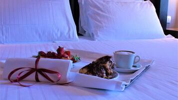 A neatly made bed with white linens, a tray with a wrapped pastry and a cup of coffee, and a pillow in the background.