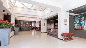 A spacious lobby with a high ceiling, a central seating area, and a dining space. - Wall Art Hotel (Prato)