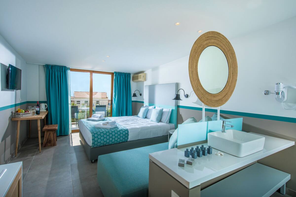 A hotel room with a bed, a desk, a bathroom with a sink and mirror, and a view of the outside.
