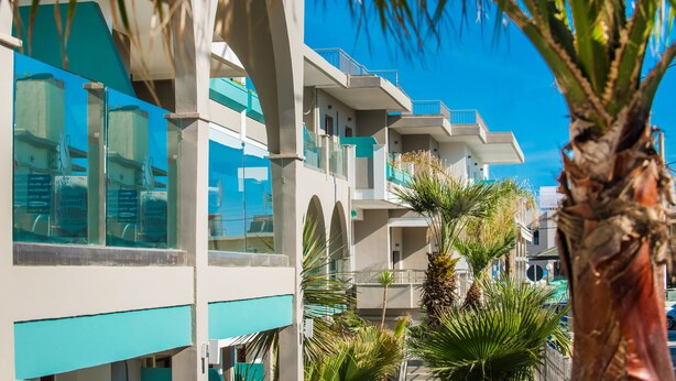 A modern hotel with multiple balconies, large windows, and palm trees. - Solimar Turquoise Adults Only - All Inclusive (Chania)