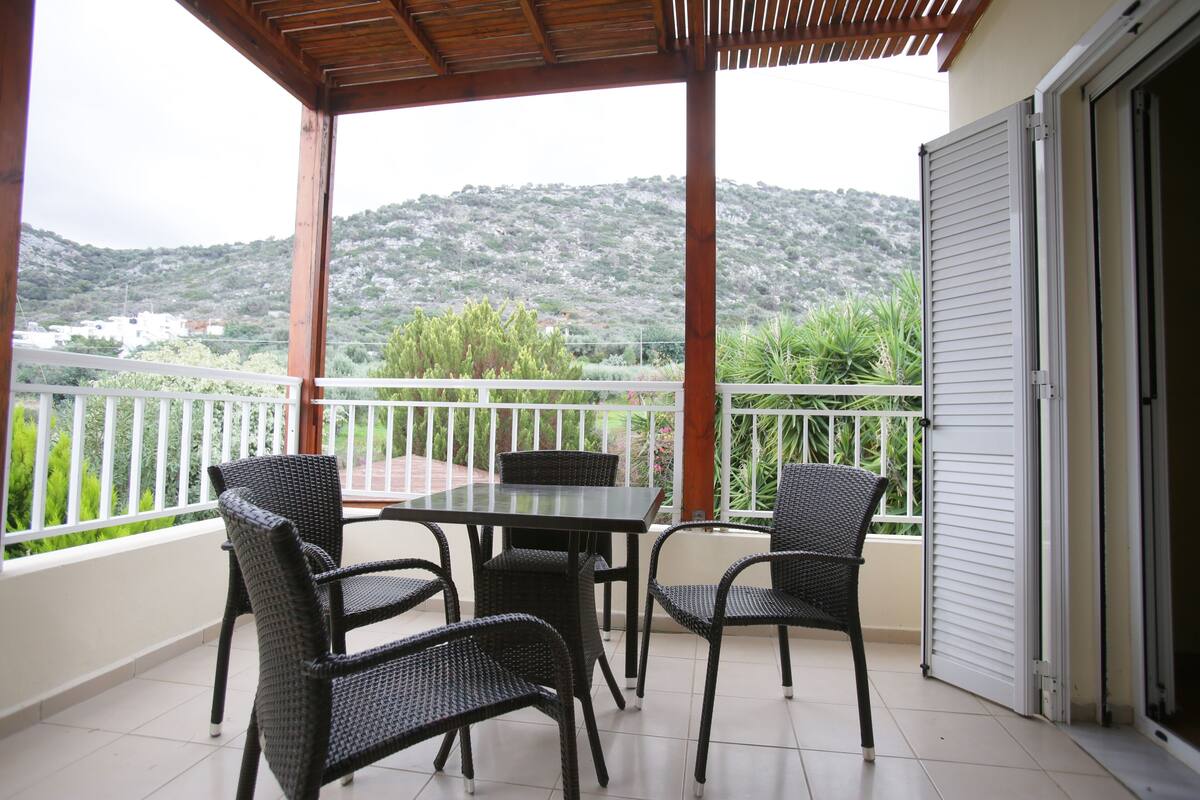 Ein Balkon mit Tisch und Stühlen, Blick auf eine hügelige Landschaft und ein weißes Geländer.