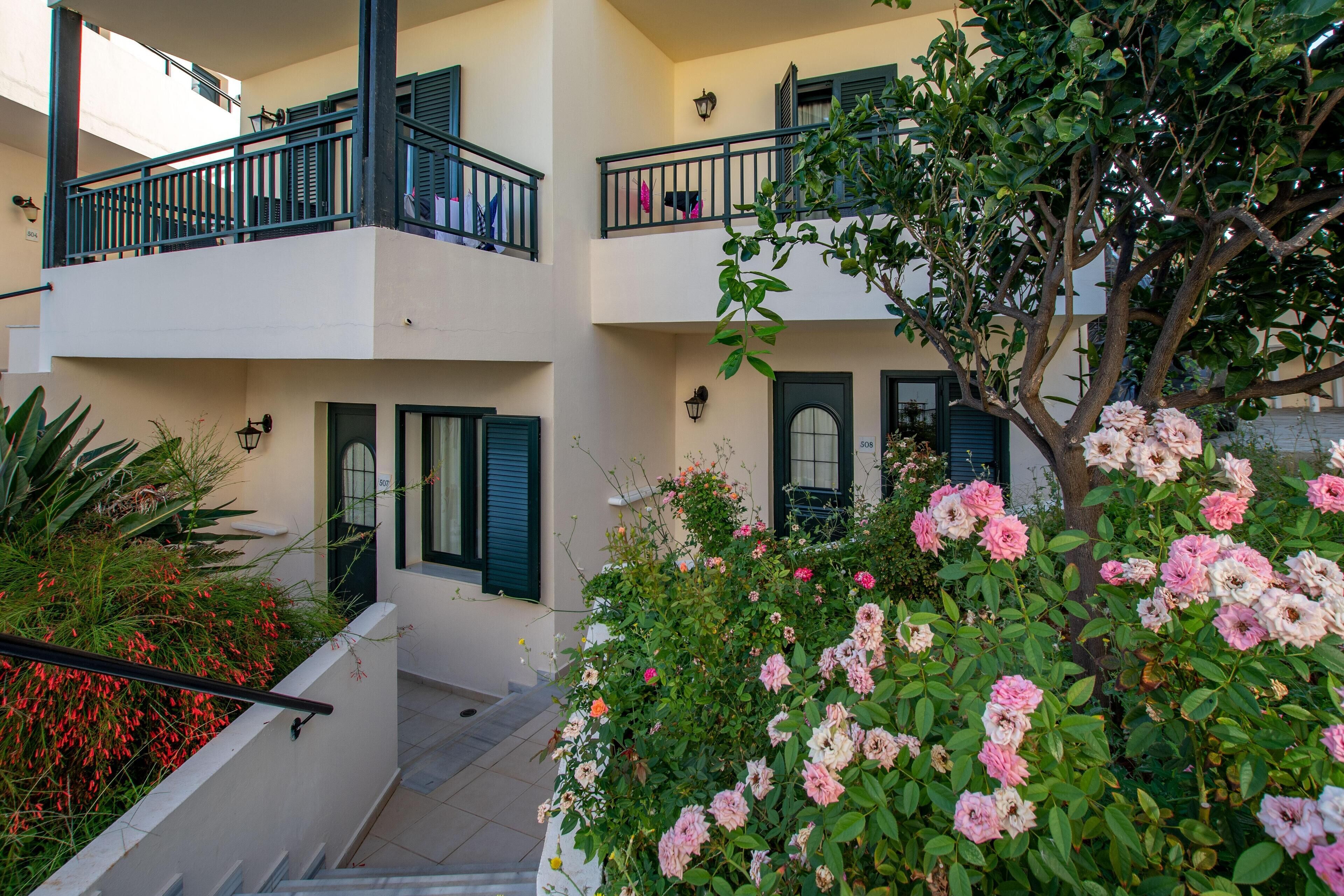 A multi-story building with balconies, a staircase, and a garden with pink flowers.