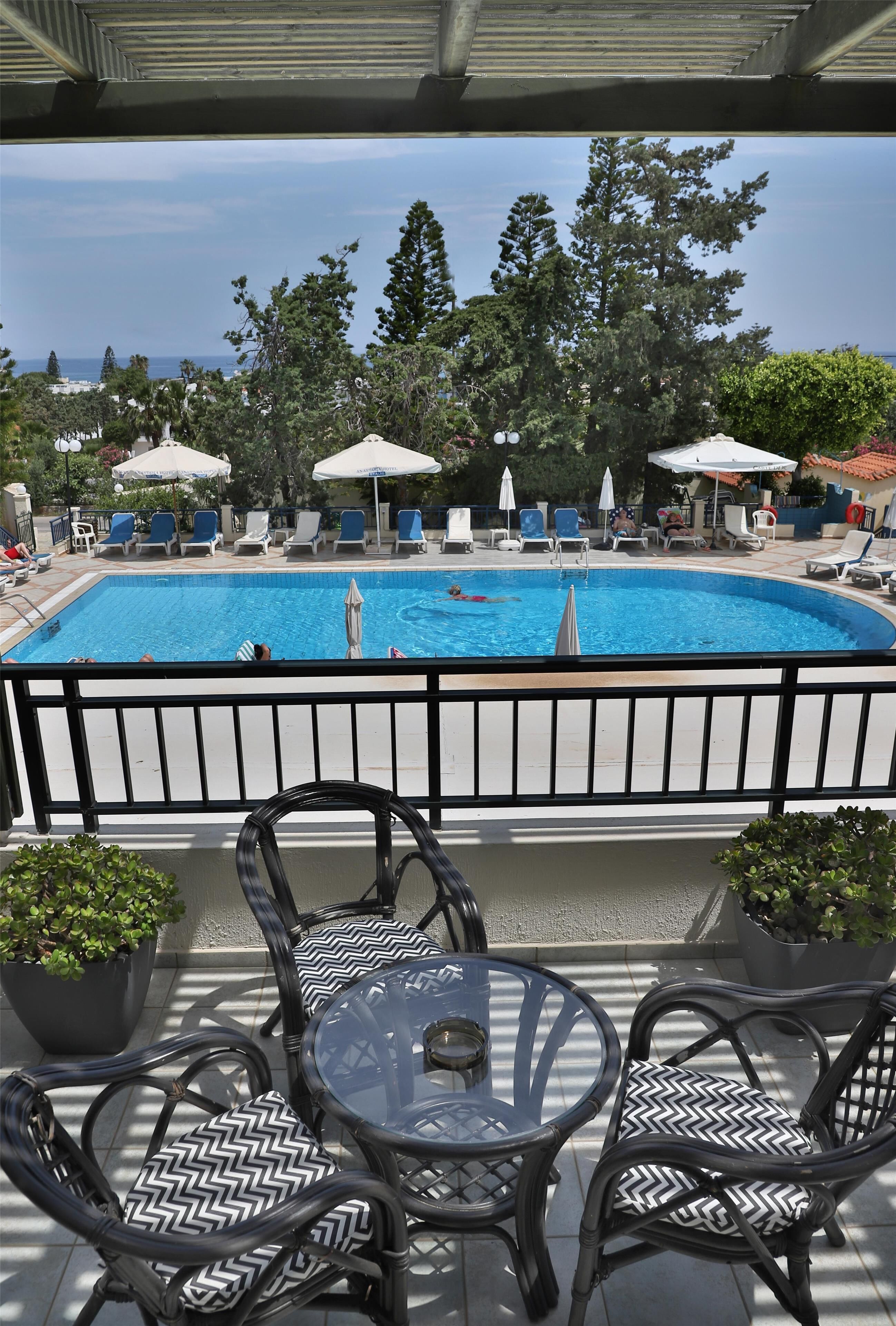 A pool area with lounge chairs and umbrellas, a glass table, and potted plants.