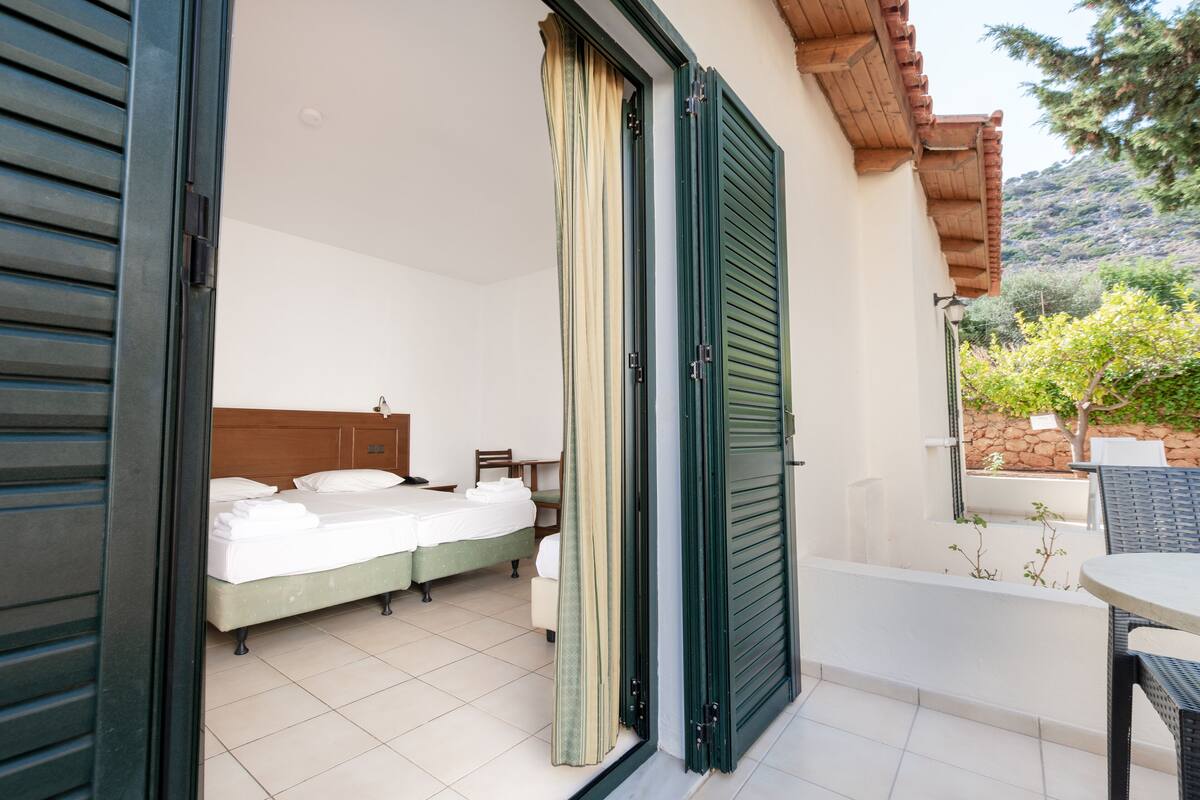 Ein Hotelzimmer mit einem Bett, einem kleinen Tisch und einem Stuhl. Ein Balkon mit Tisch und Stühlen ist vorhanden.