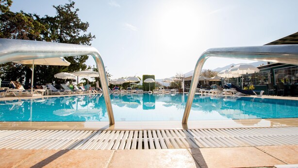 Una piscina con sillas de descanso y sombrillas, rodeada por un suelo de baldosas.