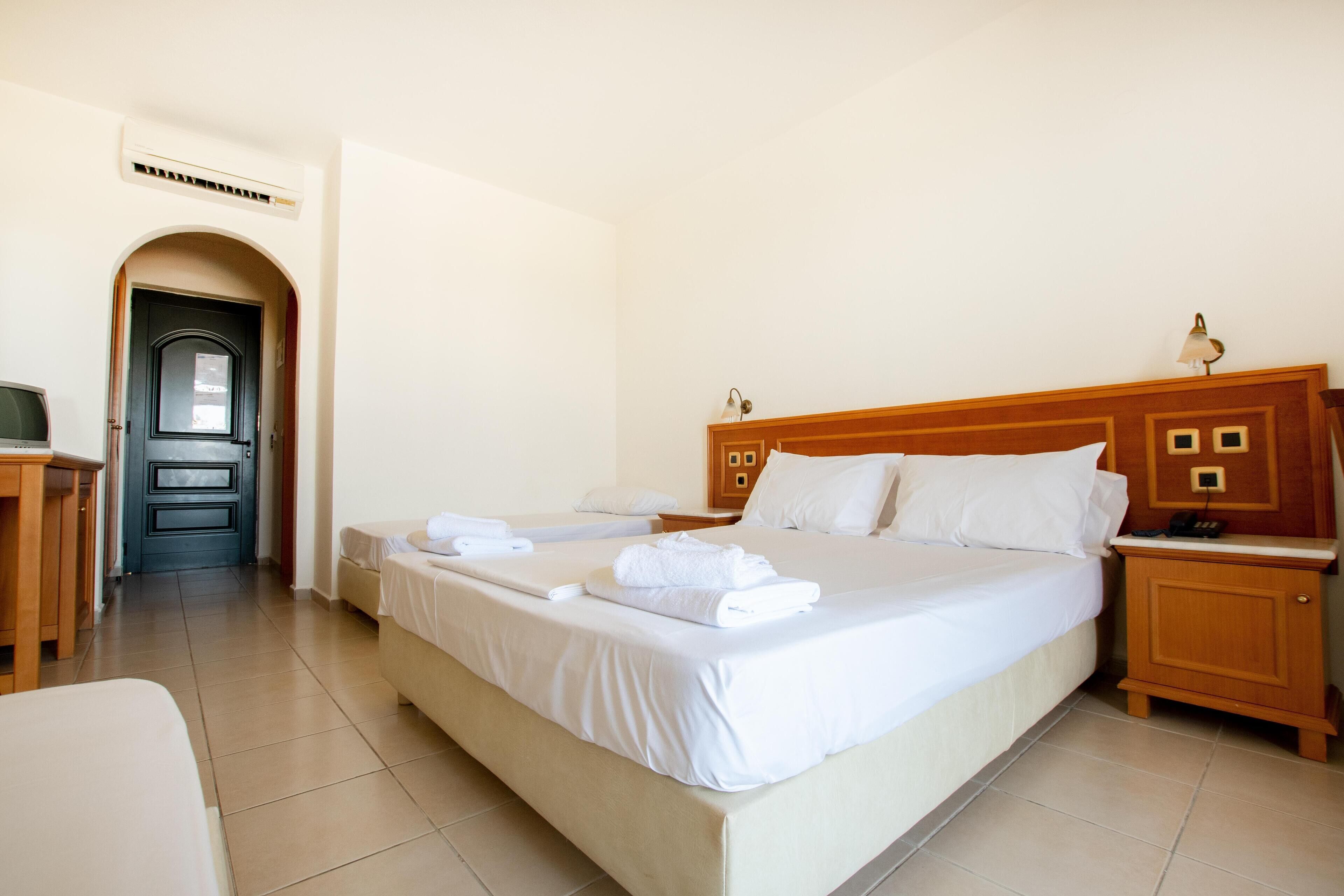 A hotel room with two beds, a wooden headboard, a nightstand, a desk, and a door leading to a hallway.