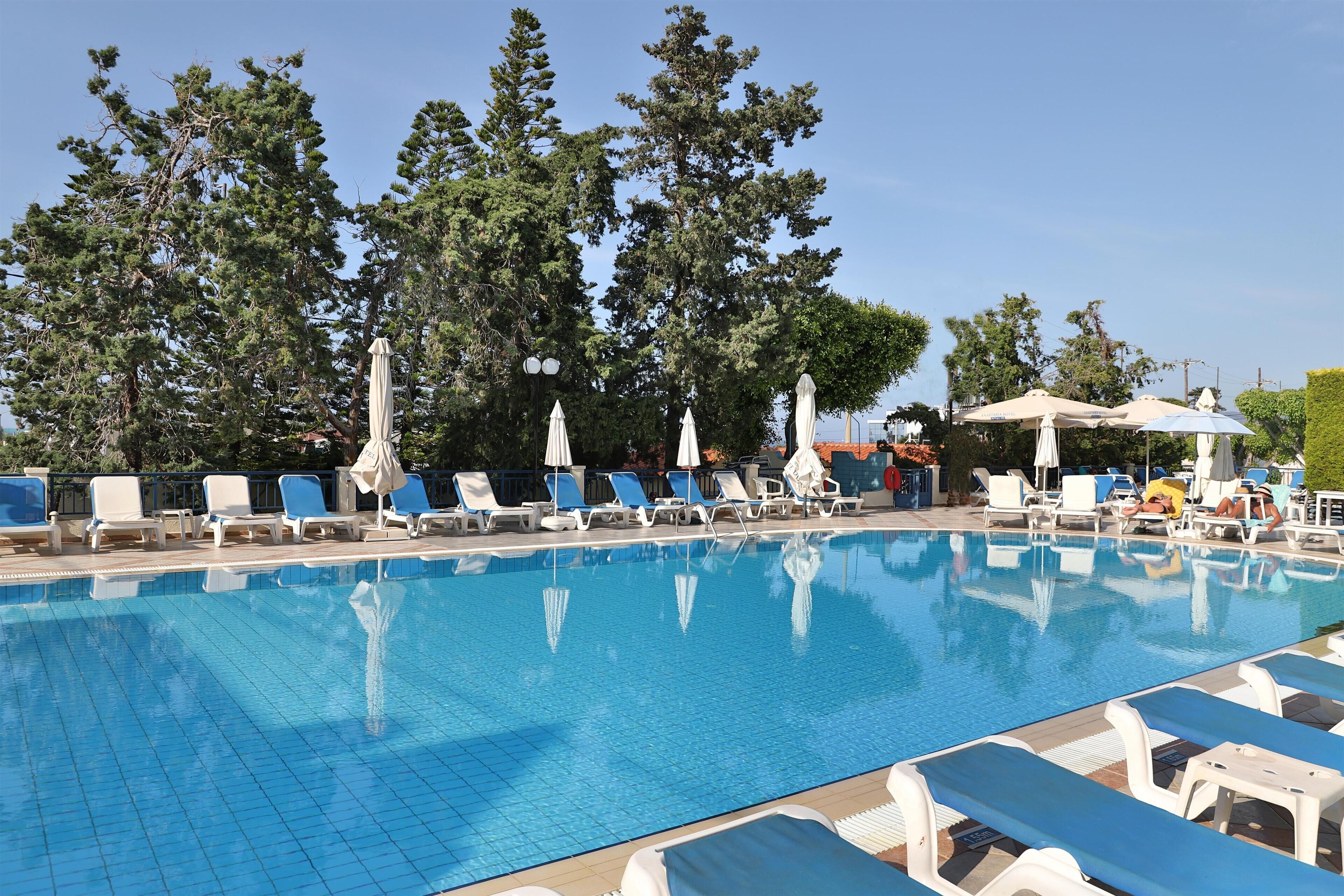 A swimming pool with lounge chairs and umbrellas, surrounded by trees.