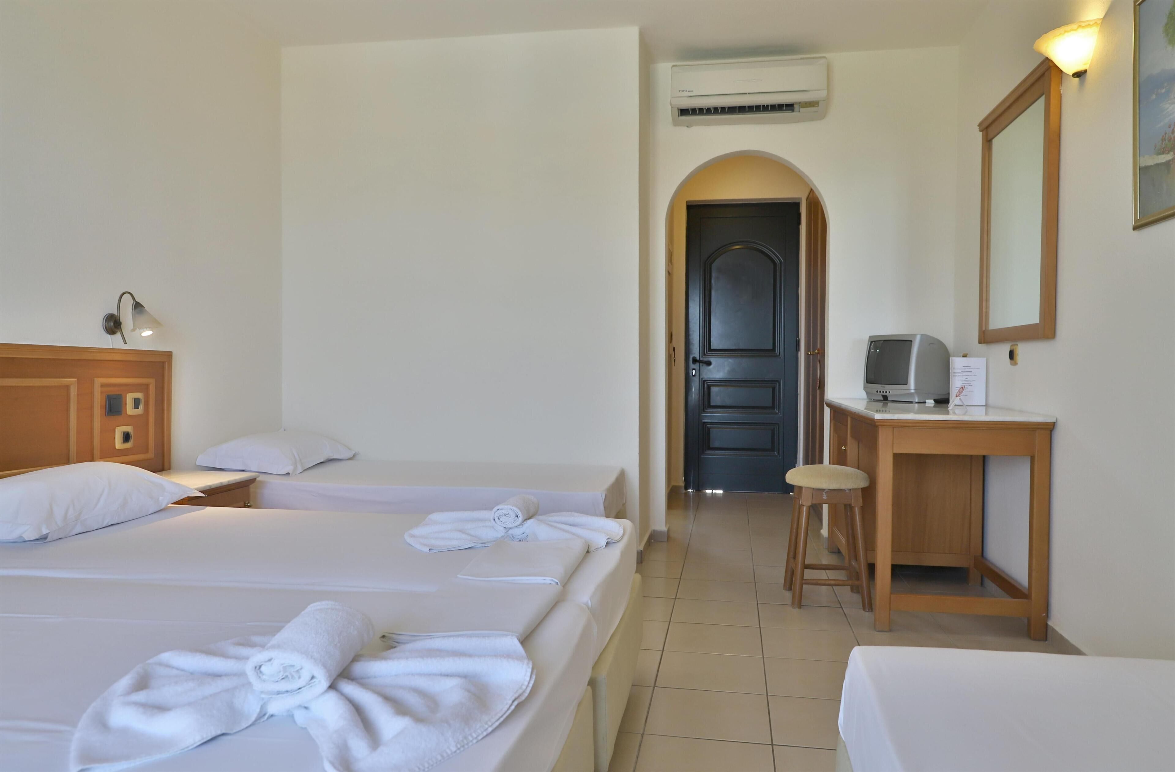 A hotel room with two beds, a desk, a chair, a TV, and an air conditioning unit.