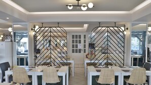 Un comedor moderno con mesas blancas y sillas de mimbre, una estructura metálica decorativa en el centro y una lámpara en el techo.
